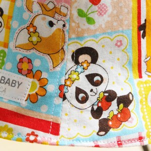 Puede incluir: Una tela colorida con un dise&ntilde;o de patchwork que presenta osos panda, un ciervo, flores y fresas. La tela tiene un fondo blanco con un dise&ntilde;o de patchwork azul, amarillo, rojo y verde. La tela tiene el texto "DAKKO BABY San Clemente, CA" en una etiqueta blanca.
