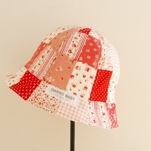 May include: A red and white patchwork baby sun hat with a label that reads "Dakko Baby".