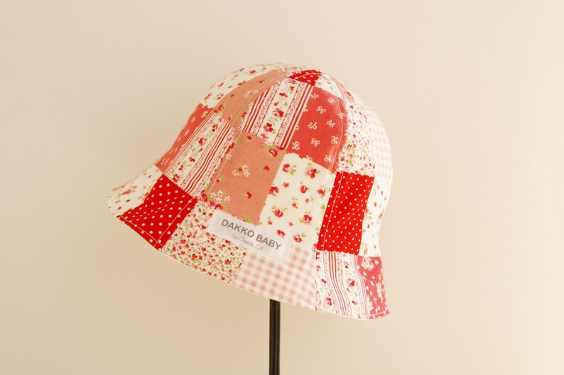 May include: A red and white patchwork baby sun hat with a label that reads "Dakko Baby".