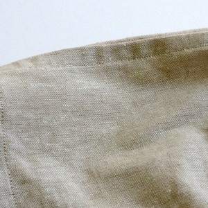 May include: Close-up of a beige linen fabric with a stitched edge. The fabric has a natural, textured look and feel.