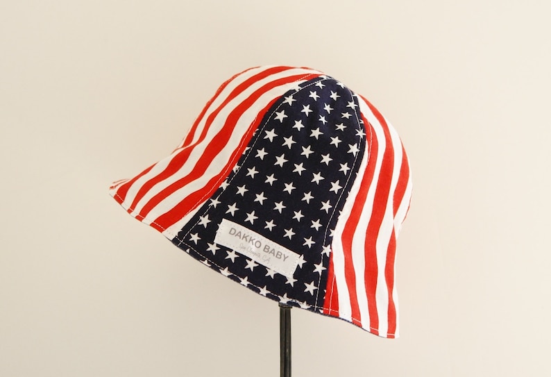 Baby summer hat, shaped like a bucket with an American flag pattern.  Red and white stripe on the side and white star on navy in the middle. The name label on it said DAKKO BABY.