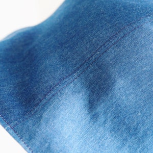 May include: Close-up of a blue denim fabric with a single seam running down the center. The fabric has a textured, woven appearance.
