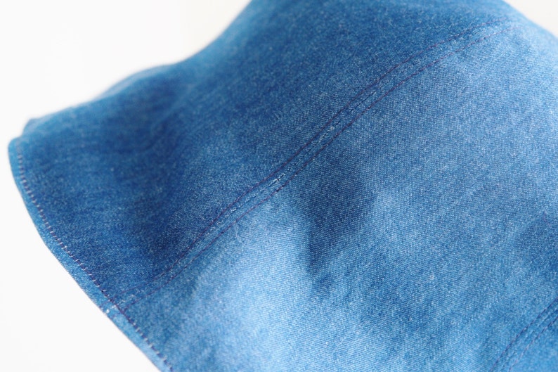 May include: Close-up of a blue denim fabric with a single seam running down the center. The fabric has a textured, woven appearance.