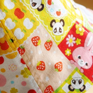 Puede incluir: Un sombrero de tela colorido con un dise&ntilde;o de patchwork que presenta fresas, flores y osos panda. El sombrero est&aacute; hecho de algod&oacute;n y tiene una combinaci&oacute;n de colores rojo, amarillo y rosa.