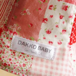 May include: A white label with the text "DAKKO BABY" and "San Clemente, CA" sewn onto a red and white patchwork fabric with floral patterns.