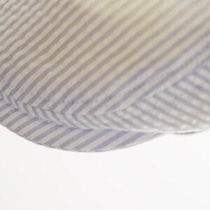 May include: Close-up of the brim of a blue and white striped hat. The hat is made of a soft, woven fabric.