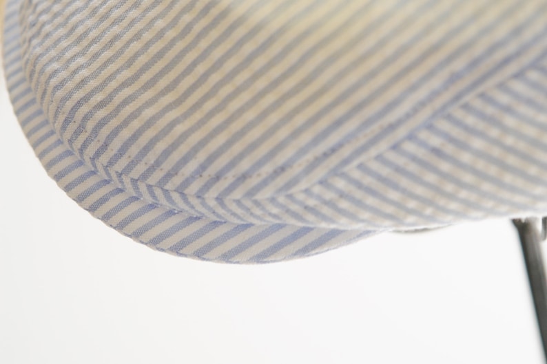 May include: Close-up of the brim of a blue and white striped hat. The hat is made of a soft, woven fabric.
