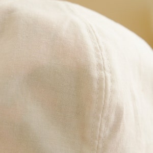 May include: Close-up of a white cotton baseball cap with a seam running down the center of the crown.