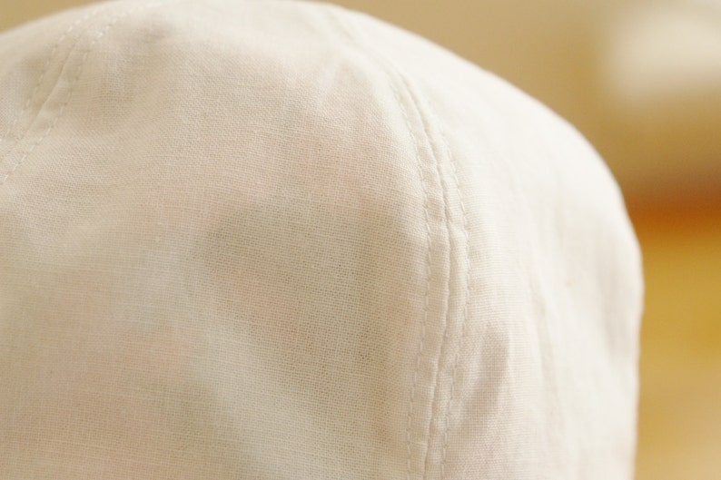 May include: Close-up of a white cotton baseball cap with a seam running down the center of the crown.