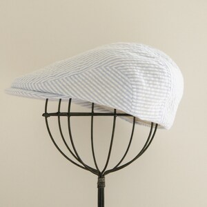 May include: A white and blue striped cotton newsboy cap on a black hat stand.
