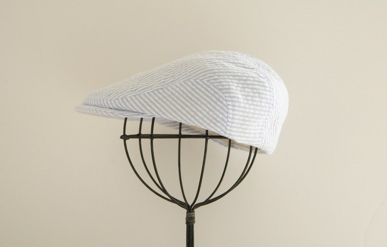May include: A white and blue striped cotton newsboy cap on a black hat stand.