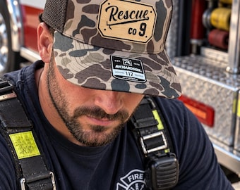 May include: A camouflage trucker hat with a brown mesh back and a tan leather-like patch on the front. The patch features the text Rescue co 9 with a graphic of a tool. A black sticker on the brim displays the text Richardson 112 Adjustable.