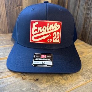 May include: Navy blue trucker hat with a red and white patch that reads "Engine co 22". The hat has a curved brim and a mesh back. The hat is adjustable and has a Richardson tag.