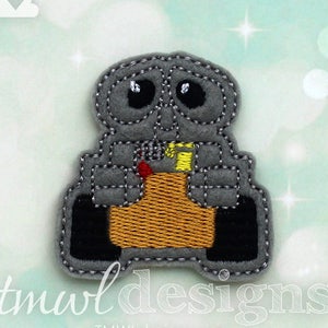 May include: A gray felt applique of a robot character with a yellow and red detail. The robot has a round body with two black wheels and a yellow detail on the front. The robot has a sad expression with two black eyes.