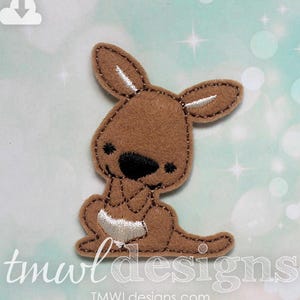 May include: A brown felt applique of a kangaroo sitting with its paws in front of it. The kangaroo has white felt accents on its ears and a black felt nose.