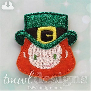 May include: A felt appliqué of a leprechaun wearing a green glitter hat with a brown buckle and a yellow letter G. The leprechaun has red hair and a white face with green eyes.