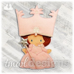 Peut inclure: Une applique en feutre représentant une fée princesse portant une couronne et une robe roses, tenant une baguette magique en or en forme d'étoile. La fée a les cheveux bruns et les yeux bleus.