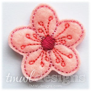 May include: A pink felt flower with a red centre and a decorative embroidered design. The flower is approximately 5 cm in diameter.