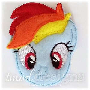 Può includere: Un'applicazione in feltro blu e bianco di Rainbow Dash di My Little Pony. L'applicazione presenta la criniera arcobaleno caratteristica di Rainbow Dash e grandi occhi espressivi.