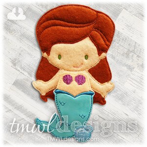 May include: A felt mermaid applique with red hair, green eyes, and a blue tail. The mermaid is wearing a seashell bra.