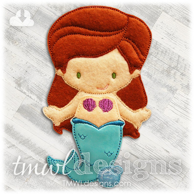May include: A felt mermaid applique with red hair, green eyes, and a blue tail. The mermaid is wearing a seashell bra.