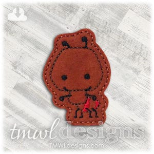 May include: A brown felt ant-shaped applique with black stitched details and a red heart. The applique has a stitched outline and is on a light wood-grain background. The text "tmwl designs" and "tmwldesigns.com" are at the bottom.