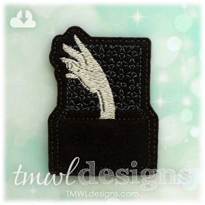 May include: Embroidered patch with a black background and a white hand reaching out of a box. The text "tmwl designs" is visible at the bottom of the patch.