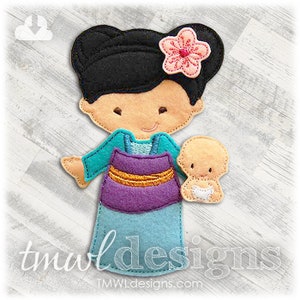 May include: A felt applique doll of a woman with black hair, wearing a blue and purple dress, holding a baby doll. The woman has a pink flower in her hair. The doll is part of a set of felt applique dolls.