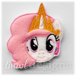 May include: Pink and white felt applique of a pony wearing a gold crown. The pony has large black eyes and a pink nose.