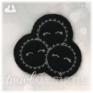 May include: Black felt applique with three black smiling faces with white stitching around the edges. The faces are arranged in a triangular shape.