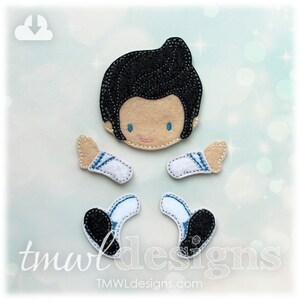 May include: Felt doll pieces with a black hair head, two arms, and two feet. The head has a tan face with blue eyes and a pink smile. The arms are white with blue accents. The feet are black and white. The text "tmwl designs" is at the bottom.