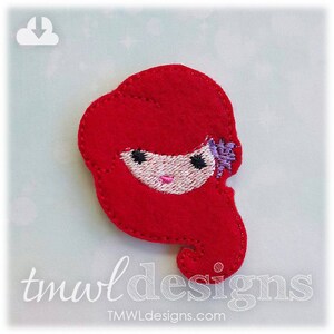 May include: Red felt applique of a cartoon girl with long red hair, a pink face, and black eyes. The girl is wearing a purple flower in her hair.