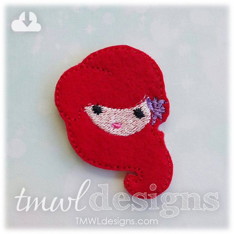 May include: Red felt applique of a cartoon girl with long red hair, a pink face, and black eyes. The girl is wearing a purple flower in her hair.