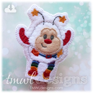 May include: A white felt finger puppet in the shape of a cartoon bee with a smiling face. The bee has red and rainbow accents, with star-shaped antennae. The puppet has the text "tmwl designs" at the bottom.