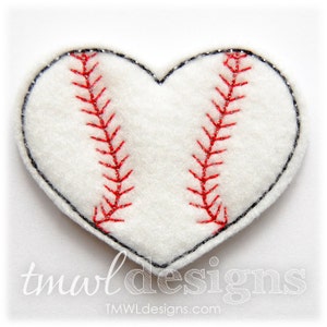 May include: A heart-shaped baseball applique with a white background. The applique features red stitching and a black outline. The text "tmwl designs" is visible in the lower left corner.