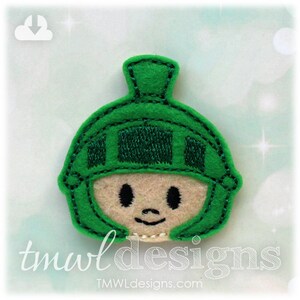 May include: Green felt applique of a cartoon character wearing a helmet. The character has a smiling face with black eyes and a small mouth.