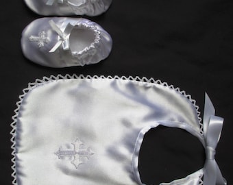 Peut inclure: Une bavette de bébé en satin blanc avec une croix brodée blanche et un nœud en satin blanc. Deux chaussures de bébé en satin blanc avec des croix brodées blanches et des nœuds en satin blanc.