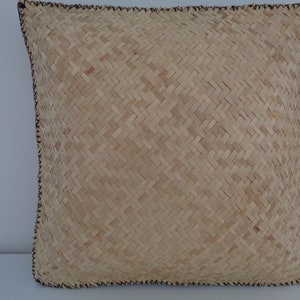May include: A natural woven cushion with a brown stitched border. The cushion is made of a light brown material with a woven pattern.