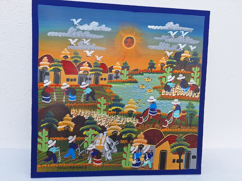 May include: A colorful painting depicting a rural scene with houses, a river, and people. The painting is done in a folk art style with bright colors and simple shapes. The sun is shining brightly in the sky, and there are birds flying overhead. The painting is signed "Tom&aacute;s Ramirez" in the lower right corner.