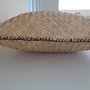 May include: A woven pillow in a natural beige colour with a black stitched edge.