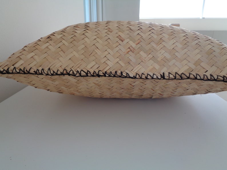 May include: A woven pillow in a natural beige colour with a black stitched edge.