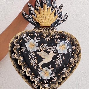 Puede incluir: Decoraci&oacute;n de pared en forma de coraz&oacute;n negro con un dise&ntilde;o floral dorado y blanco, un colibr&iacute; y una parte superior en forma de llama. El coraz&oacute;n mide aproximadamente 25 cm de ancho y 30 cm de alto.