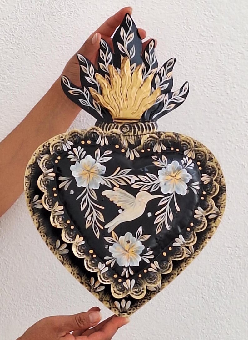 Puede incluir: Decoraci&oacute;n de pared en forma de coraz&oacute;n negro con un dise&ntilde;o floral dorado y blanco, un colibr&iacute; y una parte superior en forma de llama. El coraz&oacute;n mide aproximadamente 25 cm de ancho y 30 cm de alto.