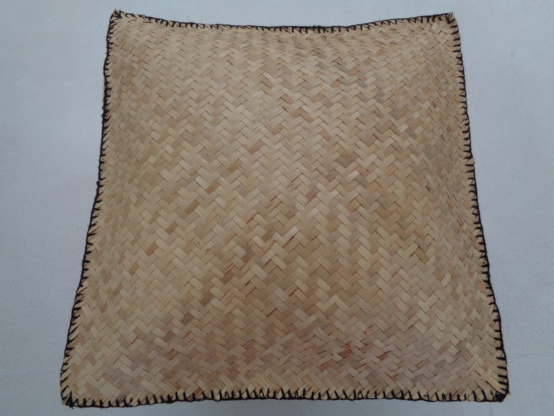 May include: A square woven cushion with a natural beige colour and a black stitched border.