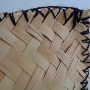 May include: Close-up of a woven basket with a black yarn border. The basket is made of natural materials and has a simple, rustic design.