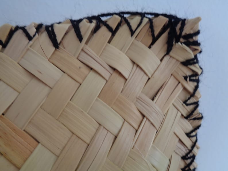May include: Close-up of a woven basket with a black yarn border. The basket is made of natural materials and has a simple, rustic design.