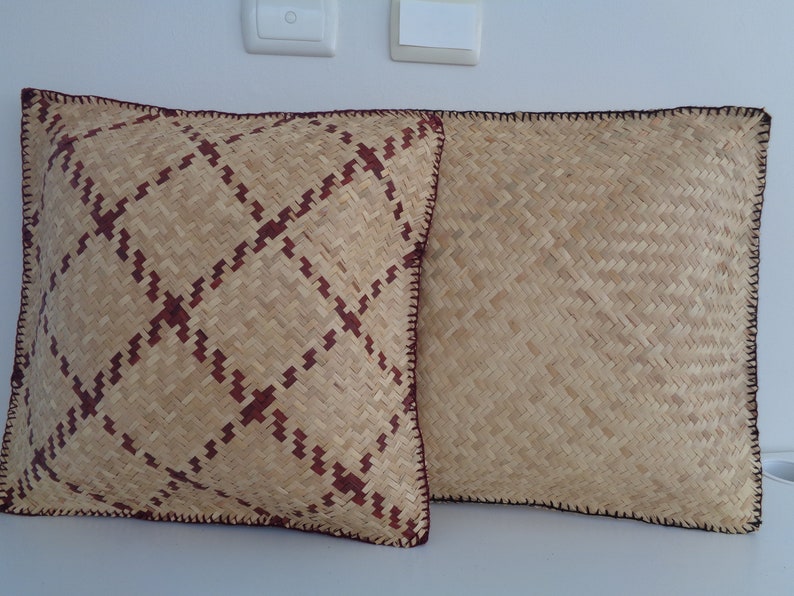 May include: Two woven cushions with a brown and beige pattern. The cushion on the left has a more intricate pattern with a red accent. Both cushions have a brown crocheted border.