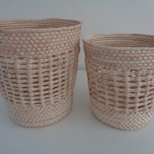 May include: Two woven baskets made of natural materials, one larger than the other. Both baskets are light brown in color and have a woven pattern.