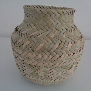 May include: A woven basket made of natural materials, with a light brown and green color scheme. The basket has a round shape and a wide opening.
