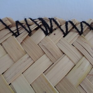 May include: Close-up of a woven straw hat with a black yarn trim around the edge.